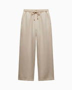 A pair of wide-leg sweatpants in a light beige or oatmeal color, featuring an elastic waistband with a matching drawstring, shown against a plain white background.