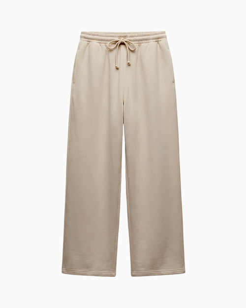 A pair of wide-leg sweatpants in a light beige or oatmeal color, featuring an elastic waistband with a matching drawstring, shown against a plain white background.