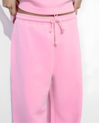 Pink sweatpants with a matching drawstring waistband, shown on a model against a plain white background.