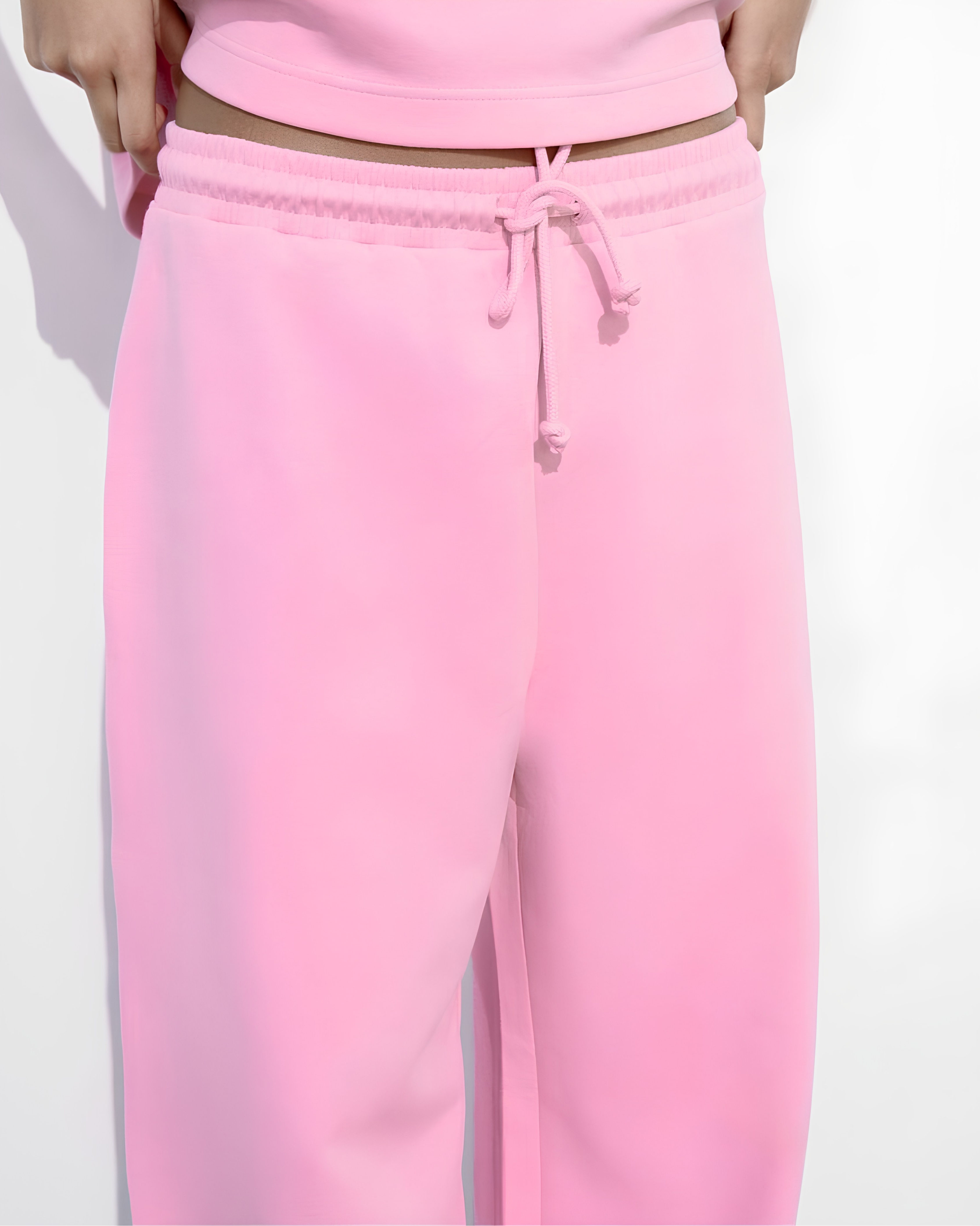 Pink sweatpants with a matching drawstring waistband, shown on a model against a plain white background.