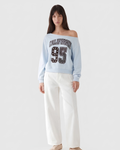 A model wearing a light blue off-the-shoulder sweatshirt with 'CALIFORNIA 95' printed on the front, paired with white wide-leg pants, against a plain light gray background.