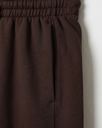 Close-up of dark brown fabric with an elastic waistband and a vertical seam, shown against a light neutral background.