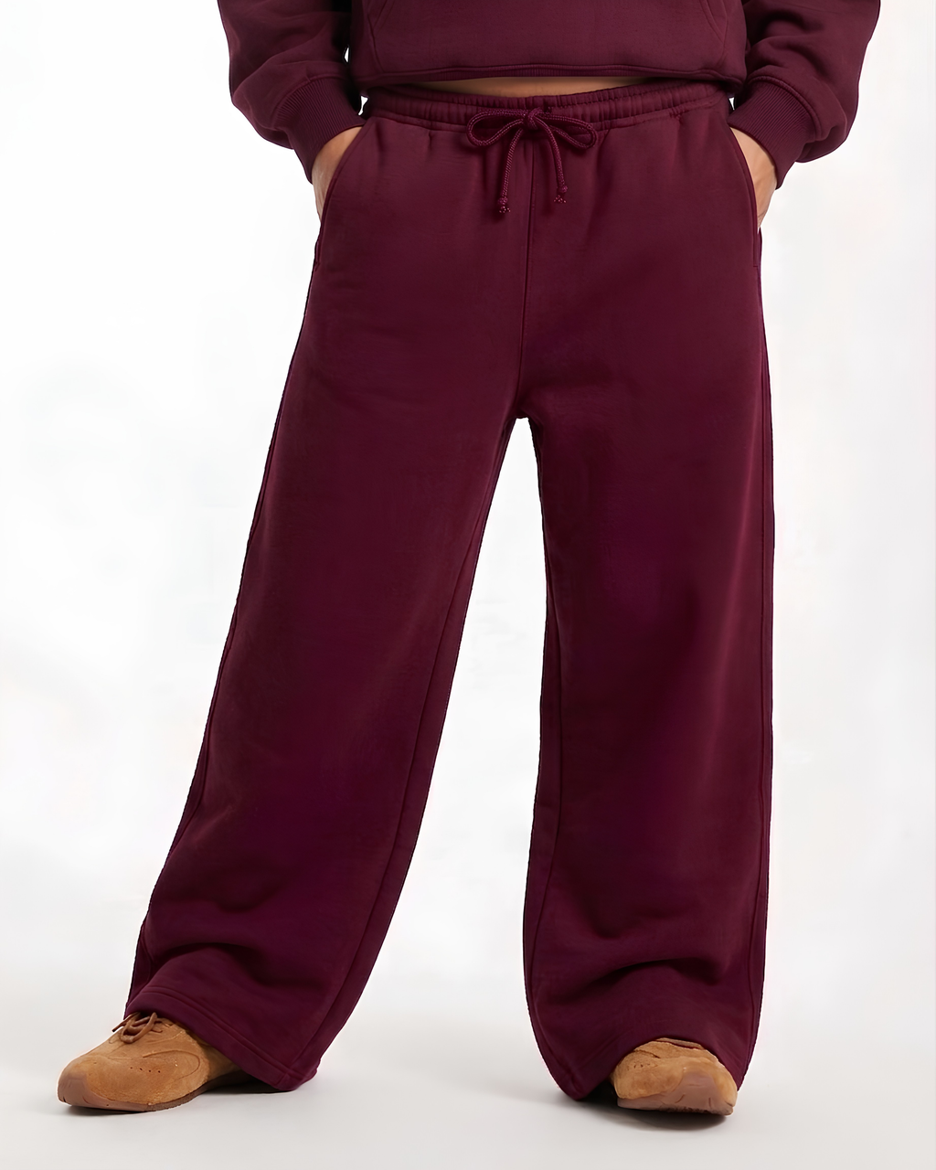 A person wearing loose, wide-leg sweatpants in a deep burgundy or plum color, paired with a matching cropped sweatshirt and tan shoes, shown against a plain white studio background.