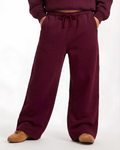 A person wearing loose, wide-leg sweatpants in a deep burgundy or plum color, paired with a matching cropped sweatshirt and tan shoes, shown against a plain white studio background.