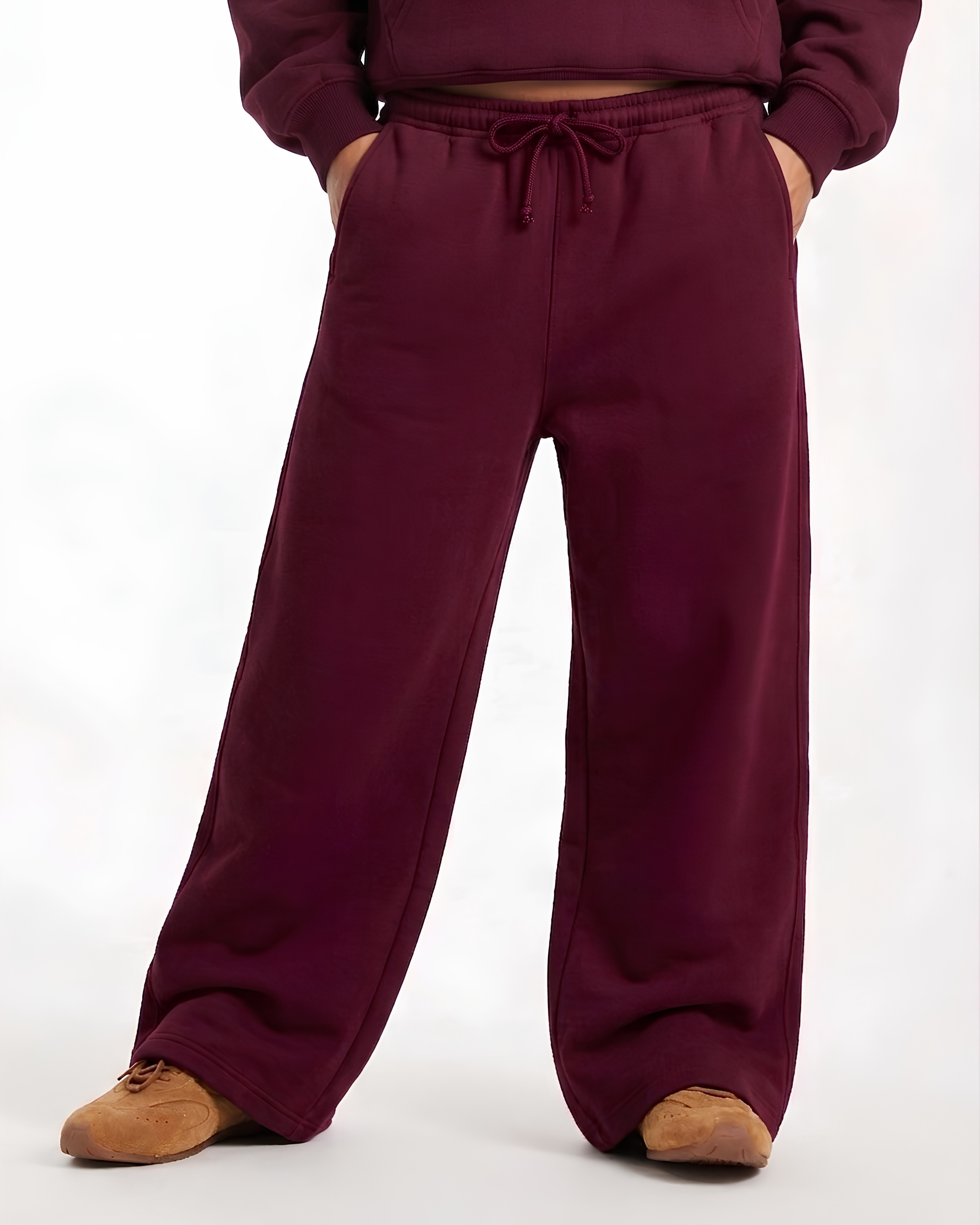 A person wearing loose, wide-leg sweatpants in a deep burgundy or plum color, paired with a matching cropped sweatshirt and tan shoes, shown against a plain white studio background.