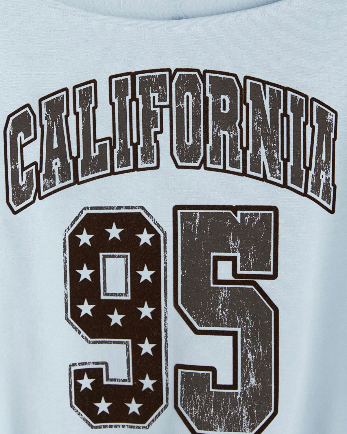 Close-up of a light blue T-shirt with a distressed dark brown graphic reading 'CALIFORNIA 95' on the chest.