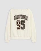 An off-white crewneck sweatshirt featuring a distressed varsity-style graphic on the front with the text 'CALIFORNIA' and the number '95' filled with stars.