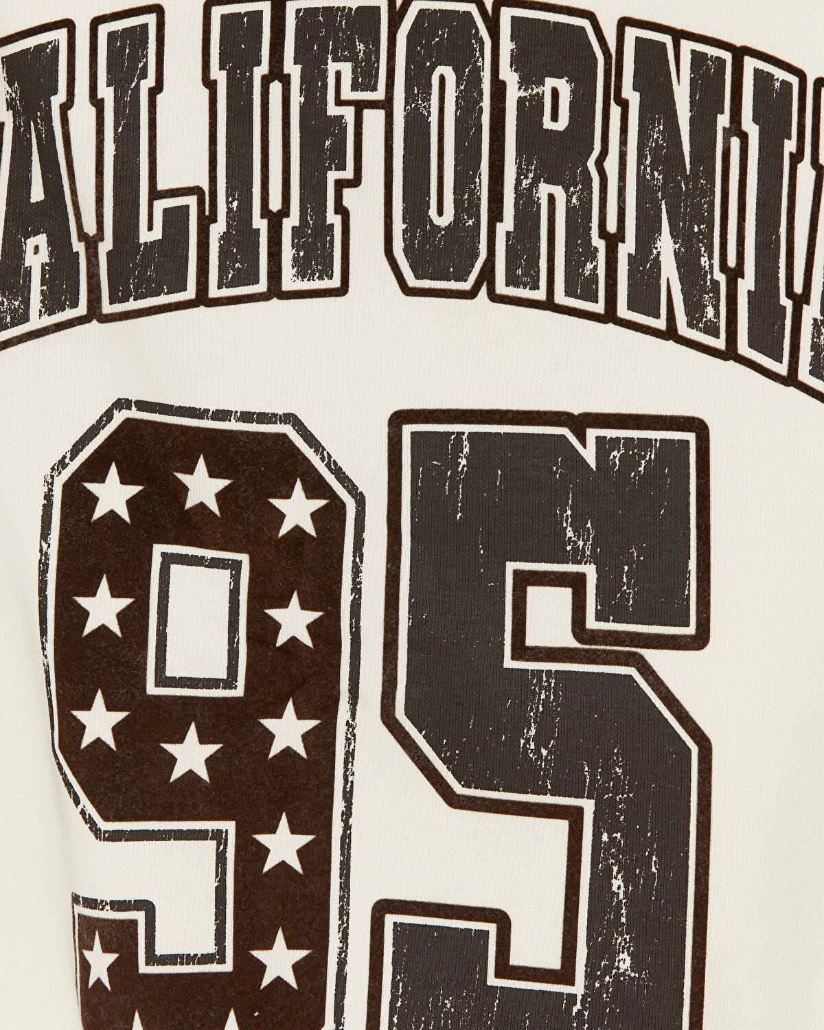 Close-up of a distressed varsity-style graphic print featuring the word 'CALIFORNIA' in arched block letters and the number '95' with white stars on a dark brown and off-white background.