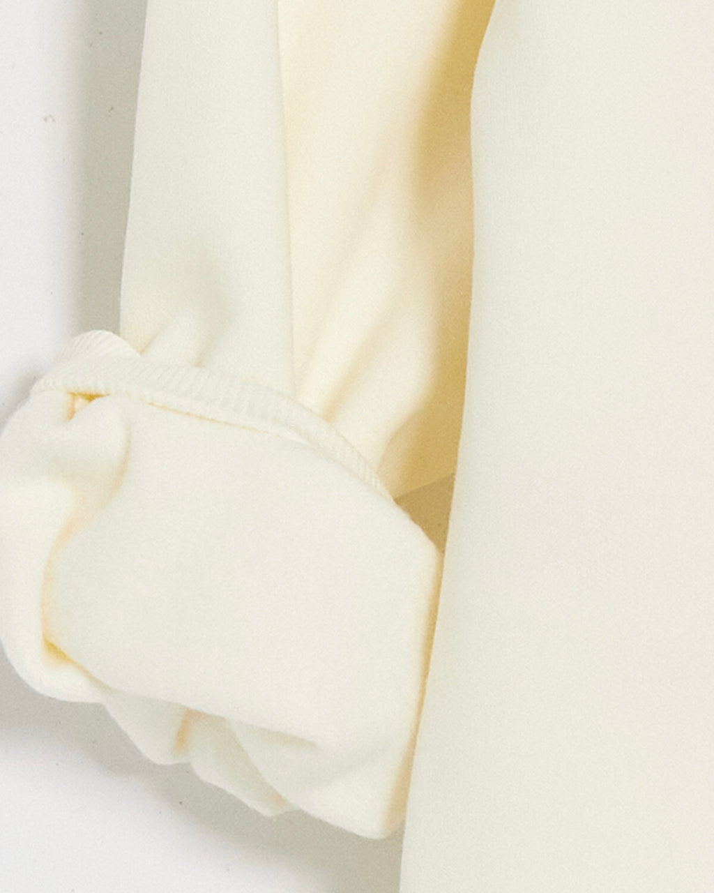 Close-up of a cream-colored knit garment, showing a folded cuff with ribbed trim and soft draped fabric.