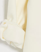 Close-up of a cream-colored knit garment, showing a folded cuff with ribbed trim and soft draped fabric.