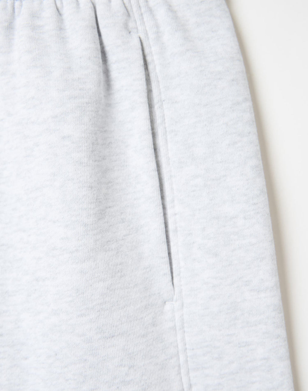 Close-up of light heather gray fabric, likely sweatpants or a soft garment, showing a vertical seam and a side pocket on a plain light background.