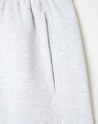 Close-up of light heather gray fabric, likely sweatpants or a soft garment, showing a vertical seam and a side pocket on a plain light background.