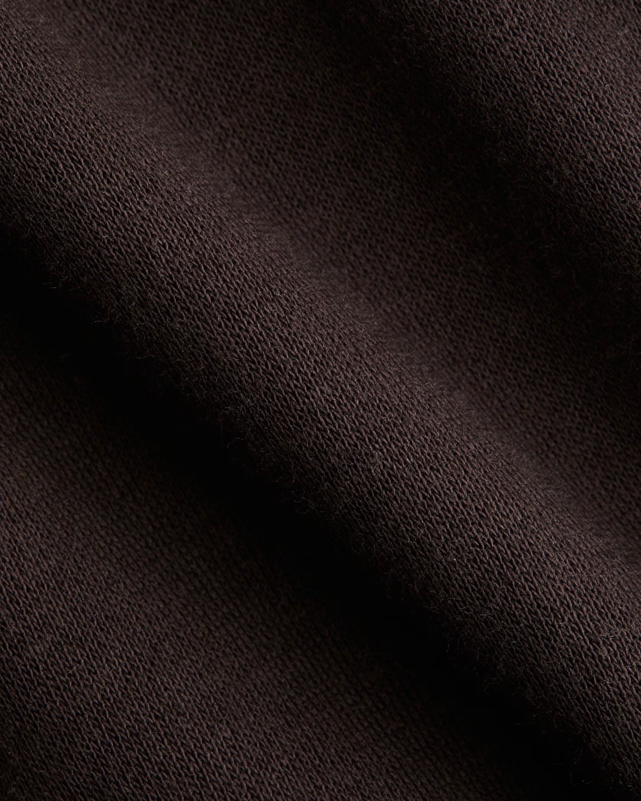 A close-up of dark brown knit fabric with soft diagonal folds showing the texture and weave.
